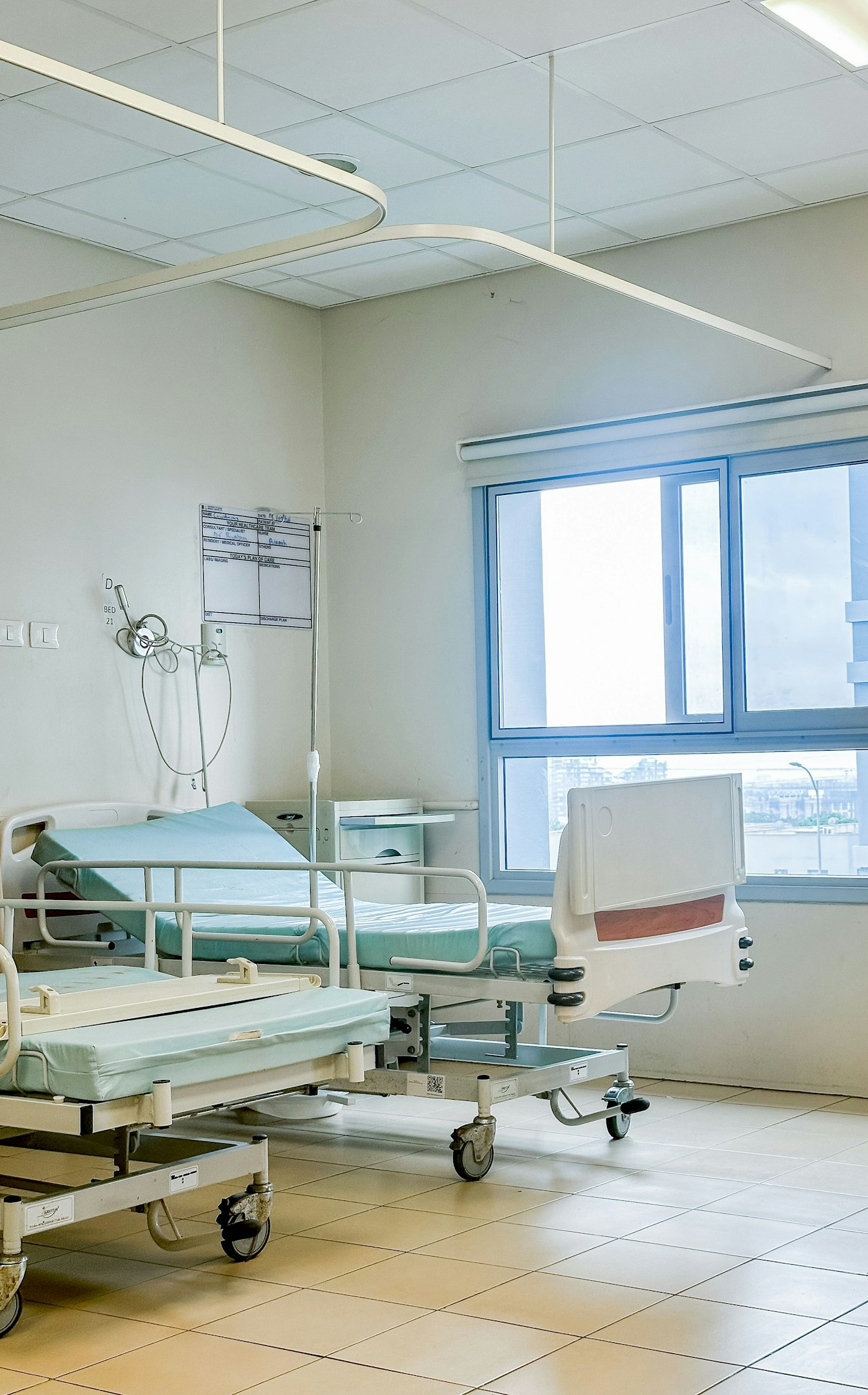 A hospital room with two made beds and a window